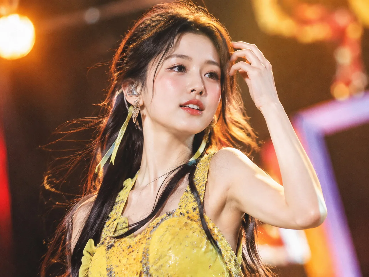 林允儿动图超清壁纸 亚洲年轻女性舞台半身照，穿亮色演出服，抬手整理发丝，舞台灯光偏暖，动感抓拍